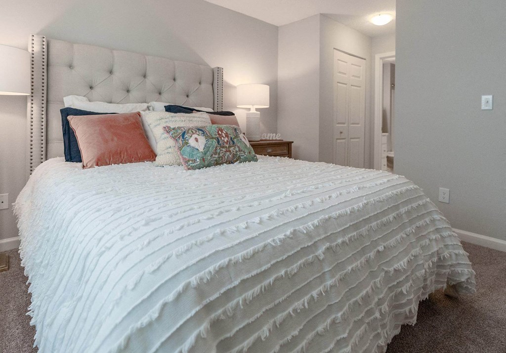 A bed with a white comforter and pillows in a room.