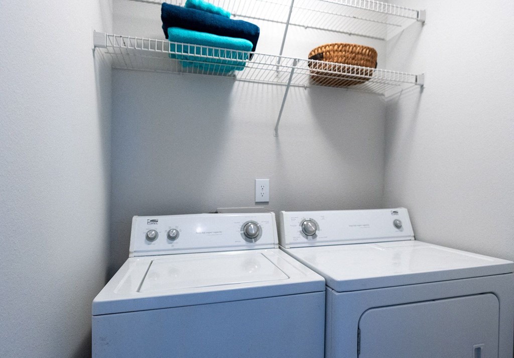 Two washing machines are in a laundry room with towels hanging above them.