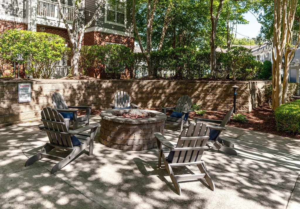 A fire pit surrounded by chairs in a sunny backyard.