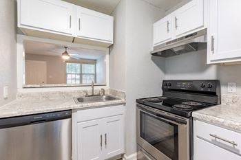 A kitchen with a stove, sink, and cabinets.