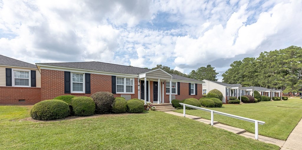 A row of houses with green lawns and white fences.