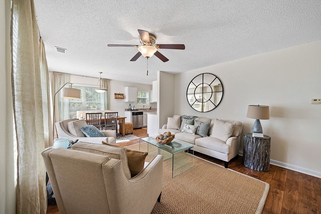 A living room with a beige couch, a glass coffee table, and a ceiling fan.