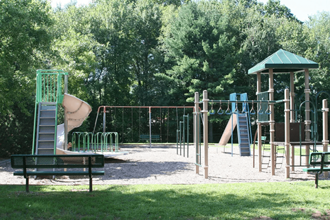 A playground with a green slide, swings, and a wooden structure.