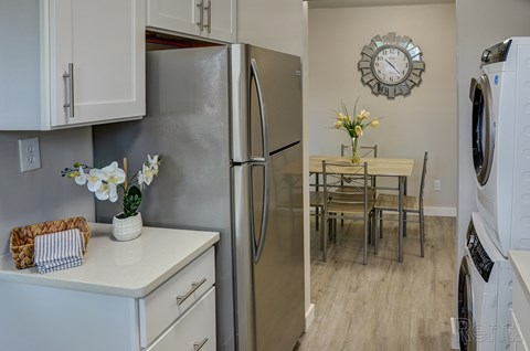 A kitchen with a refrigerator, a washing machine, and a dining table with chairs.
