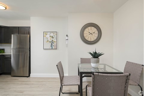 A modern kitchen with a glass table and chairs, a fridge, and a clock on the wall.