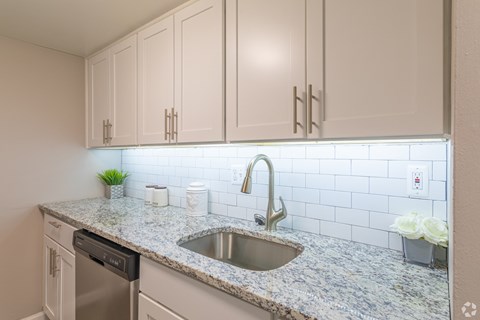 A kitchen with a granite countertop and a stainless steel sink.