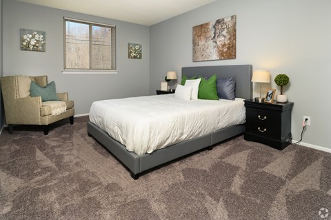 A bedroom with a large bed, a chair, and a painting on the wall.