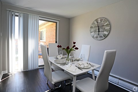 A dining room with a table set for two and a clock on the wall.
