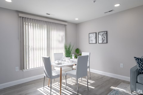 A dining room with a table set for two and a potted plant on the windowsill.