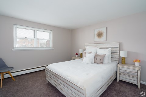 A bedroom with a large bed, a chair, and a nightstand with a lamp.