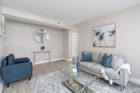 A living room with a grey couch, a blue armchair, and a glass coffee table.
