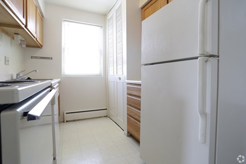 A white refrigerator stands in a kitchen with wooden cabinets and a stainless steel dishwasher.
