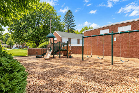 A playground with swings and a slide in front of a brick building.