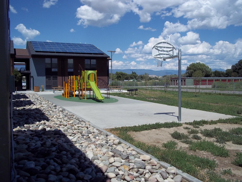 blue sky with clouds and a basketball court and playground in front of apartment building