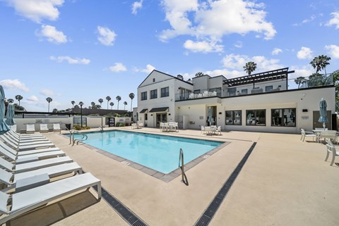 A swimming pool with sun loungers and a building in the background.