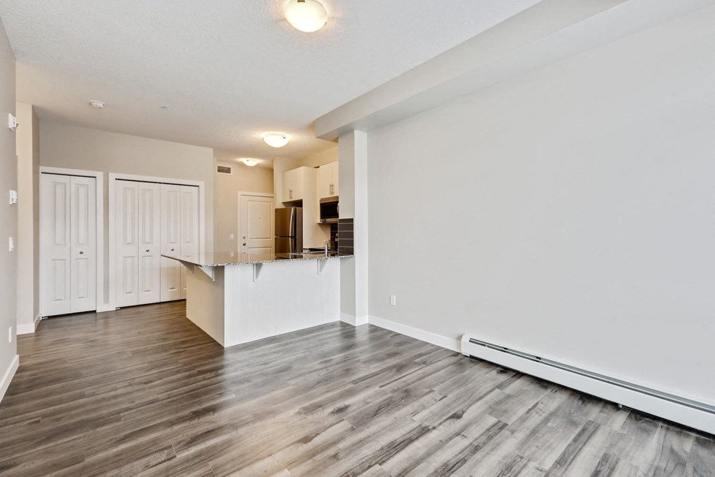 an empty living room and kitchen with wood flooring and white walls