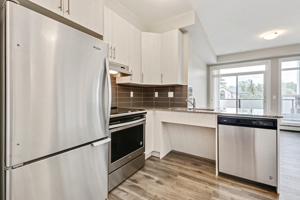a white kitchen with stainless steel appliances and a window