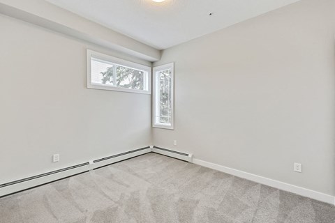 an empty living room with two windows and white walls