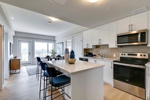 a kitchen with white cabinets and a large white island with blue chairs at shawnessy station