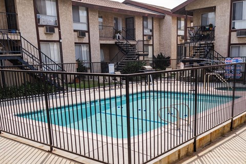 A black fence surrounds a small pool in front of apartment buildings.