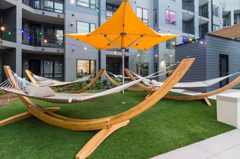 A yellow umbrella is attached to a hammock in a grassy area.