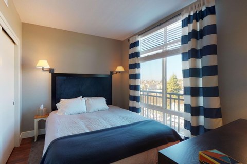 A bedroom with a large bed and a window with striped curtains.