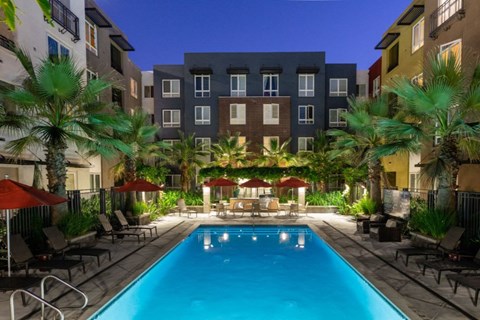 A swimming pool surrounded by lounge chairs and umbrellas in a courtyard