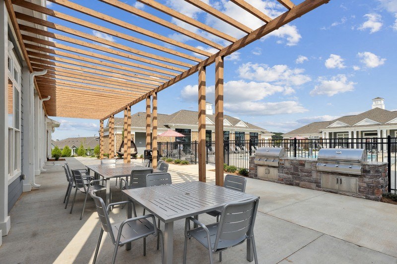a patio with tables and chairs and a grill with a house in the background