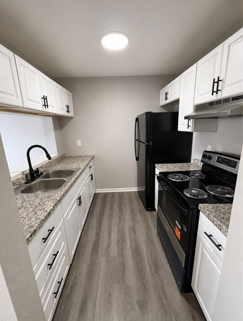 A black refrigerator sits in a kitchen with white cabinets and a granite countertop.