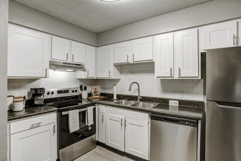 A kitchen with white cabinets and black countertops.