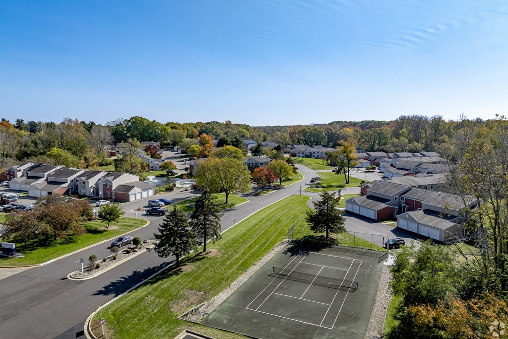 A tennis court is located in the middle of a grassy area in a residential neighborhood.