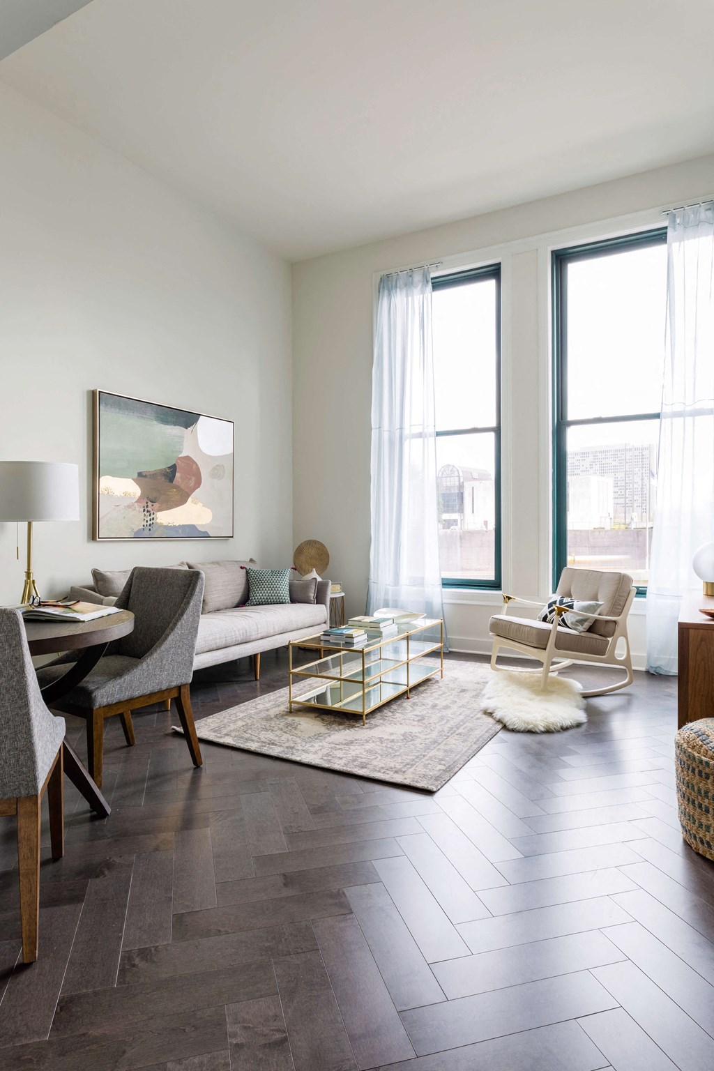 A modern living room with a grey sofa, a wooden dining table and chairs, a rug, and a painting on the wall at The Pennsylvanian Apartments, Pittsburgh, 15222