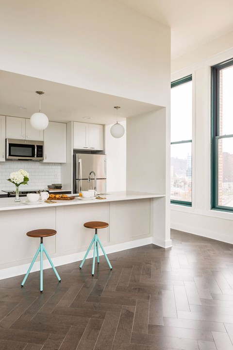A kitchen with a white counter and two blue stools.