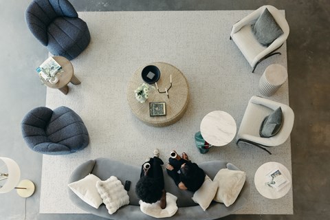 Two people sitting on a grey couch in a living room with a coffee table and a grey pouf.