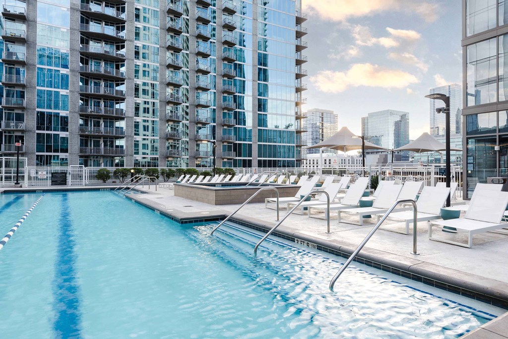 A swimming pool with lounge chairs and a view of a city skyline.