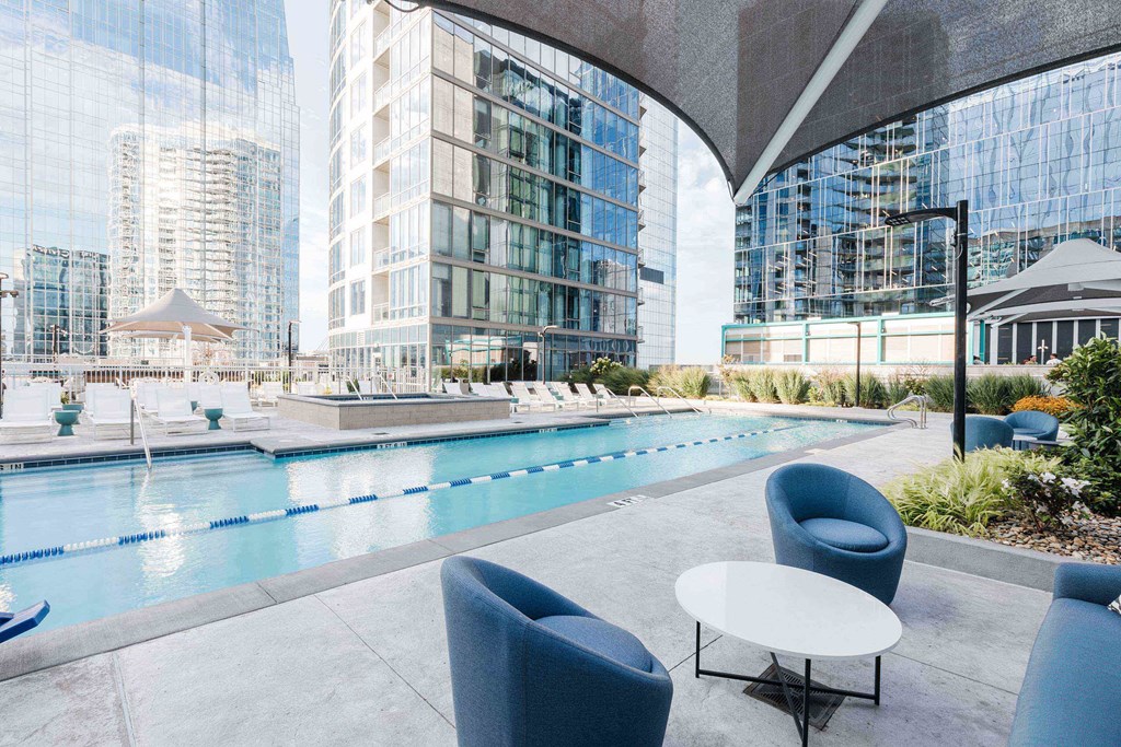 A pool area with chairs and a table in the foreground and a building in the background.