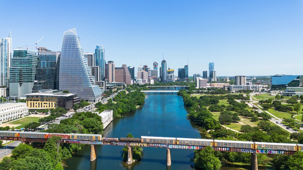 A train is crossing a bridge over a river in a city.at Placemakr Downtown Austin, Austin