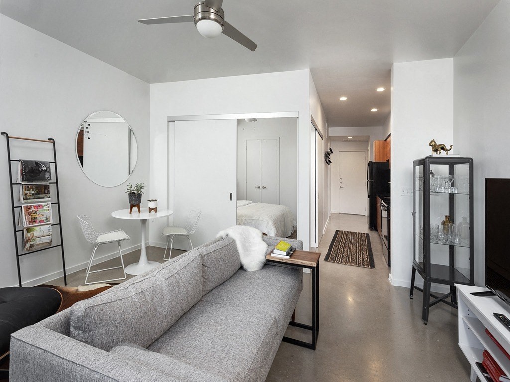 a living room with a couch and a table and a hallway with a bed