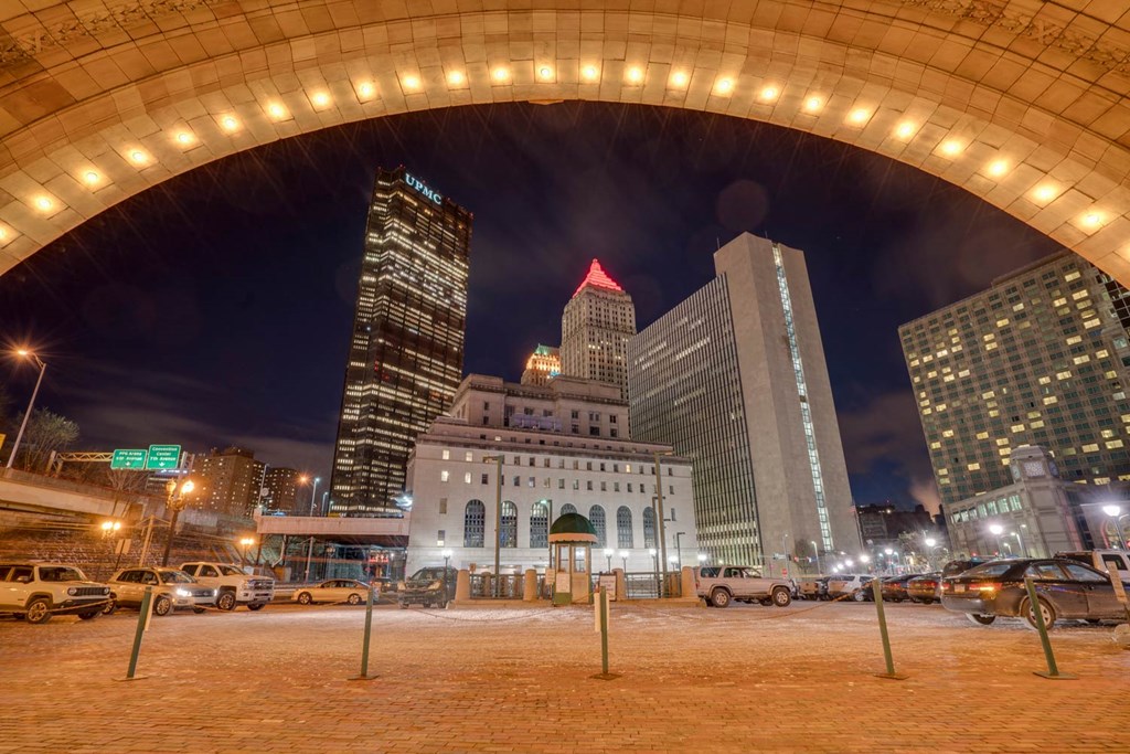 A cityscape at night with a large archway in the foreground at The Pennsylvanian Apartments, Pittsburgh, PA, 15222