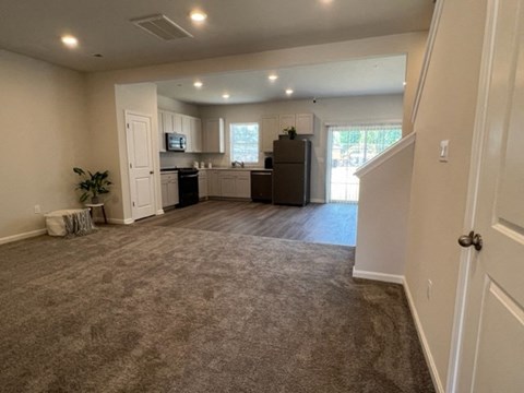 an empty living room and kitchen with a carpeted floor