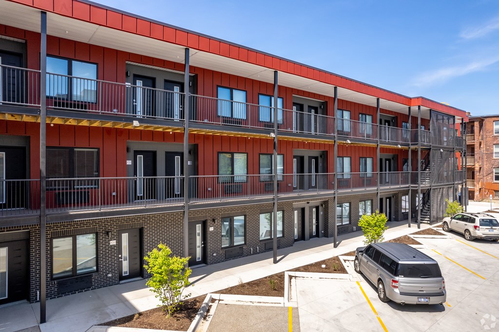 A red and white building with a balcony and a tree in front.