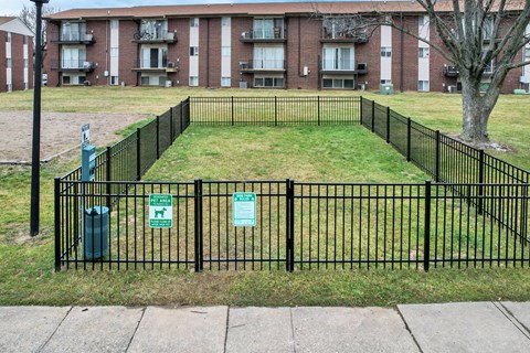 A black fence surrounds a grassy area in front of a brick apartment building.