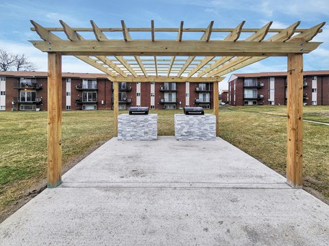 A wooden pergola structure is in the foreground with apartment buildings in the background.