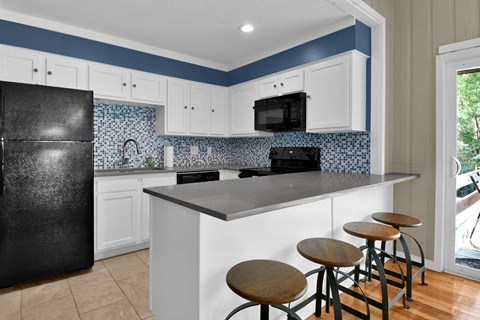 A kitchen with a black refrigerator and white cabinets.
