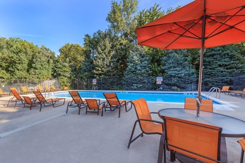 A pool area with orange chairs and a red umbrella.