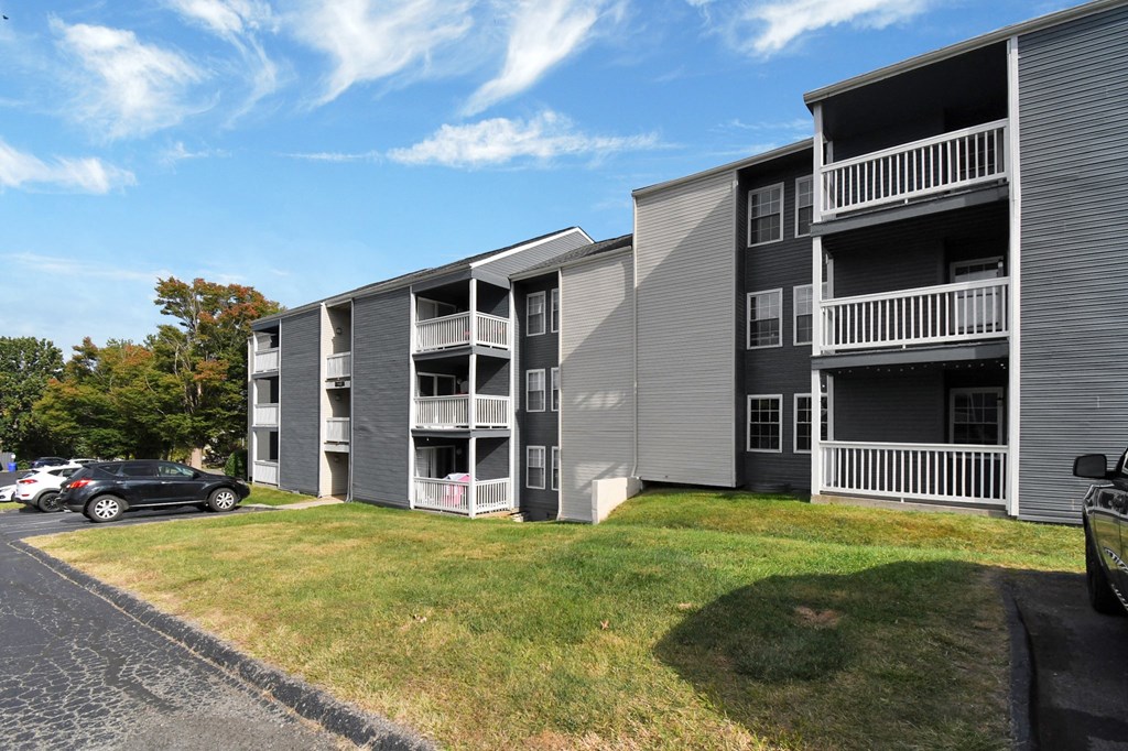 an exterior view of a grey apartment building with balconies and a green lawn