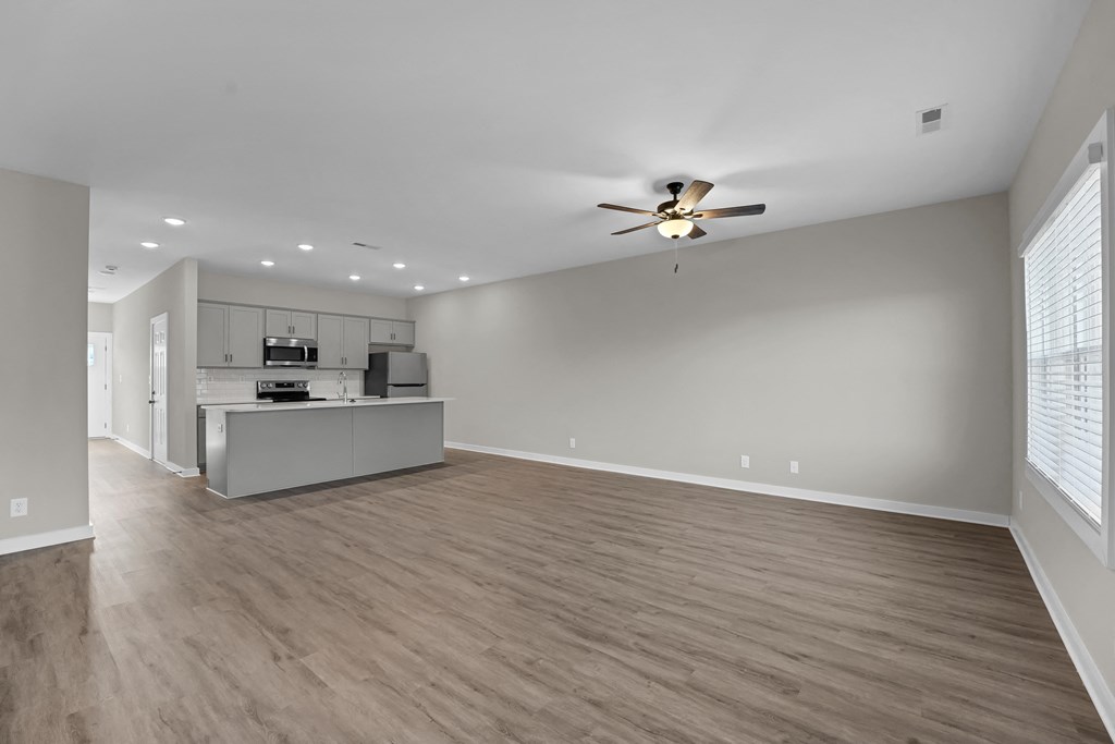 an empty living room with a ceiling fan and a kitchen