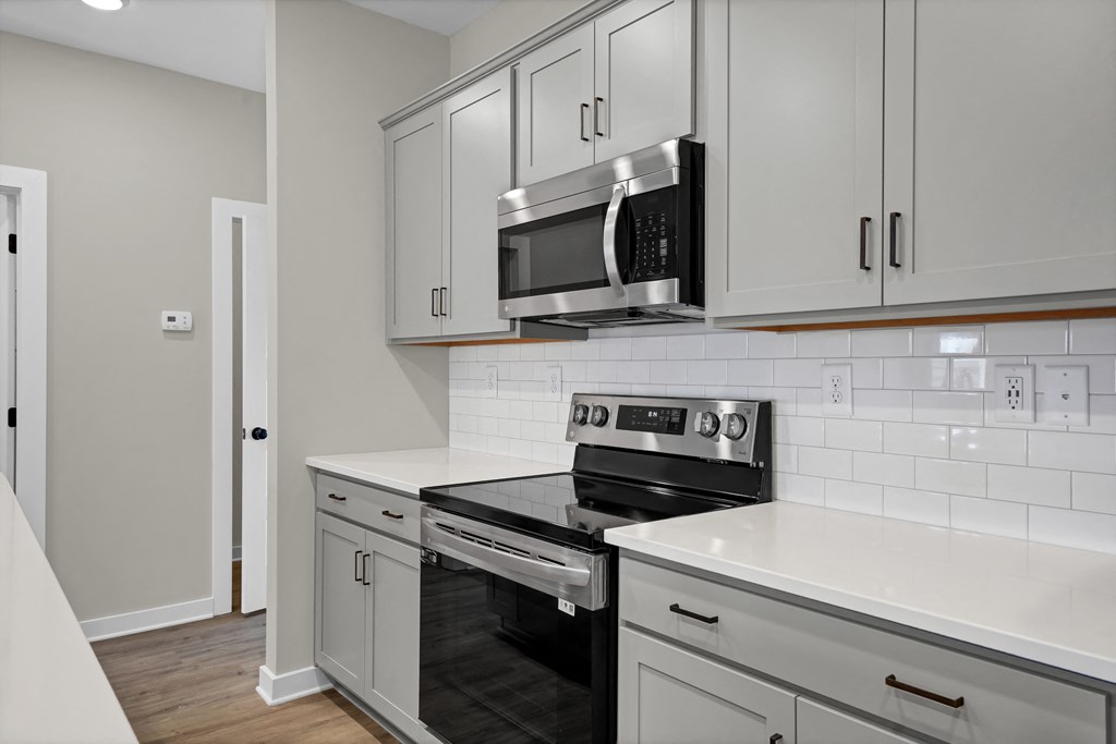 an empty kitchen with white cabinets and a stove and microwave