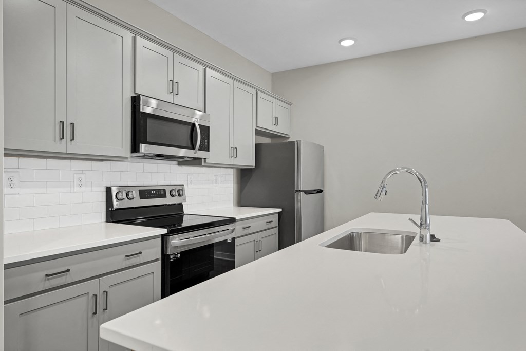 an empty kitchen with white counter tops and a sink