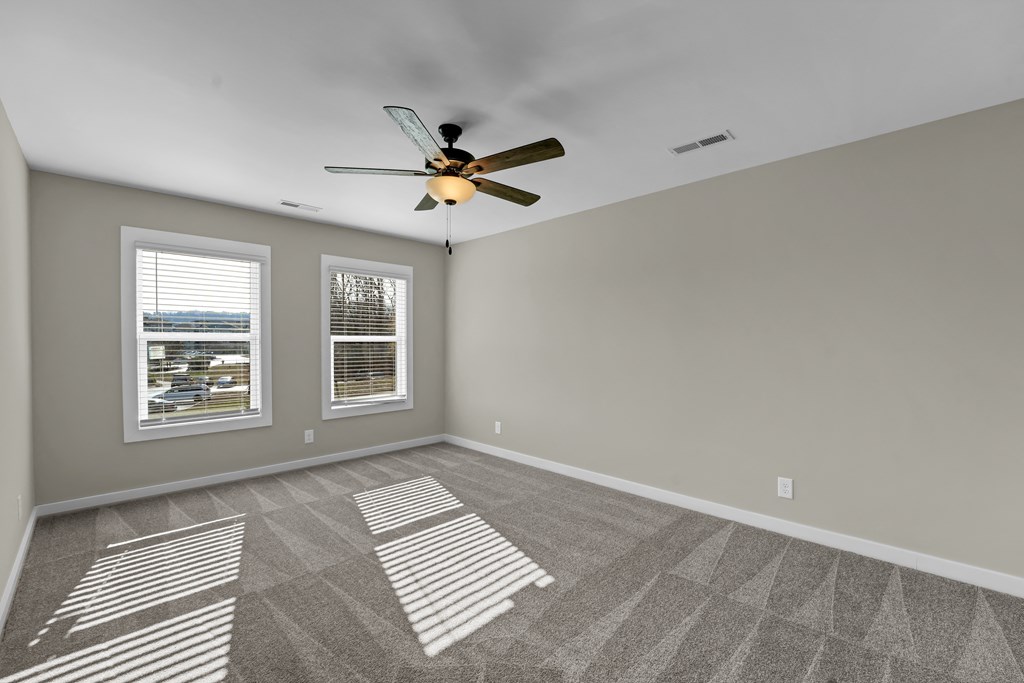 an empty living room with a ceiling fan and two windows